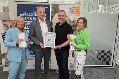 Vorsitzender Kai Leimig vom Elternverein (im schwarzen Shirt) überreicht die Patenschaftsurkunde an die Volksbank-Direktoren René Lorenz und Brigitte Klinger (links, mit Avatar). Rechts ist Spendenpraktikantin Sanny Raphael mit Maskottchen zu sehen.