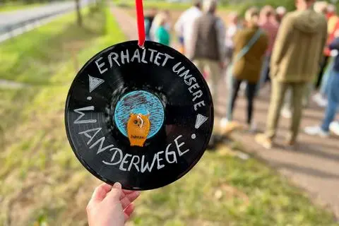"Erhaltet unsere Wanderwege": In der Nähe der Stelle, wo Spaziergänger die B 8 am Ortsrand von Lindenholzhausen überqueren und jetzt über eine neu angebrachte Leitplanke (links) klettern müssen, hängt als Protestnote diese umfunktionierte Schallpatte.