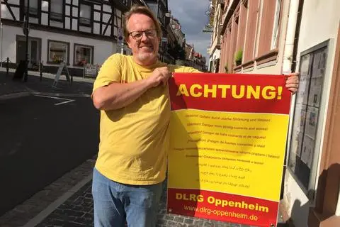„Achtung!“: Andreas Lerg, Vorsitzender der DLRG-Ortsgruppe, zeigt eines der Plakate, die jetzt am Oppenheimer Strandbad mehrsprachig vor den Gefahren des Badens im Rhein warnen. Foto: Ulrich Gerecke