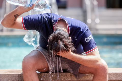 Ein Mann kühlt sich an einem Springbrunnen mit Wasser ab. Symbolfoto: dpa