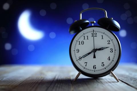 Ein Wecker zeigt die Uhrzeit kurz nach halb drei. Dahinter scheint der Mond - es ist also mitten in der Nacht.