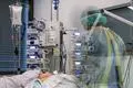 Ein Pfleger steht auf der Corona-Intensivstation neben einem Patienten, der an einem ECMO-Gerät hängt.