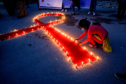 Eine Frau stellt auf einer Veranstaltung im Vorfeld des Welt-Aids-Tags Kerzen auf, die eine rote Schleife formen - ein weltweit anerkanntes Symbol für die Solidarität mit HIV-Infizierten. Der jährliche Welt-Aids-Tag wird von der Weltgesundheitsorganisation (WHO) der Vereinten Nationen ausgerufen. Archivfoto: dpa/Sunil Pradhan