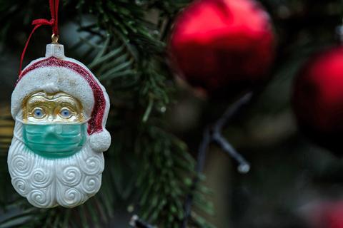 Ein Weihnachtsmann mit Mund-Nasen-Schutz hängt als Baumschmuck an einem Weihnachtsbaum.
