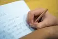 Ein Grundschüler sitzt an einem Tisch und schreibt mit einem Bleistift in sein Heft.