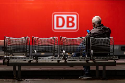 Das Logo der Deutschen Bahn (DB) prangt an der Seite einer Lok, während ein Mann auf dem Hauptbahnhof wartet. Foto: dpa