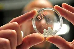 Ein Forscher der Boehringer Ingelheim Deutschland GmbH hält eine Petrischale mit einem fertigen Medikament in Pillenform hoch.